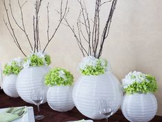 four white vases with green and white flowers in them are sitting on a table