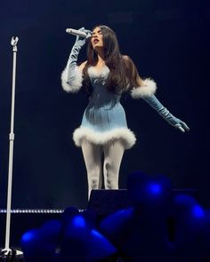 a woman in a blue dress and white fur coat singing into a microphone on stage