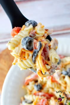 a spoon full of pasta salad with black olives and tomatoes on it, ready to be eaten