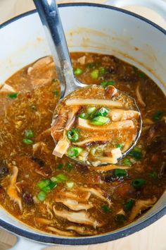 a ladle full of soup with meat and vegetables in it is being held by a spoon