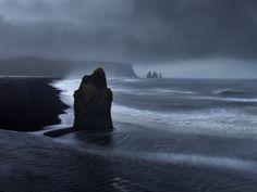 an image of the ocean with rocks in the foreground and dark clouds above it