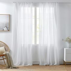 a living room with white curtains and a wicker chair