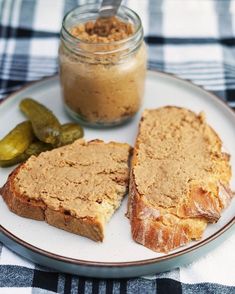 two pieces of bread on a plate with pickles and peanut butter next to it