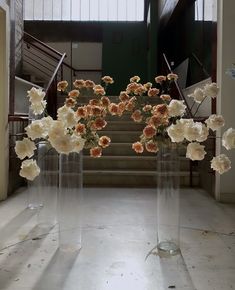 three clear vases filled with flowers on top of a white tiled floor next to stairs