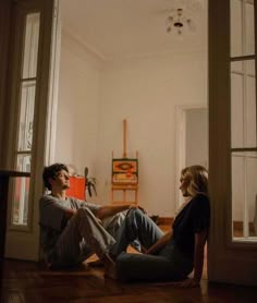 two people sitting on the floor in front of an open door and looking at each other