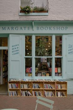 a book store with many books in the window and on display outside, there is a green chair next to it