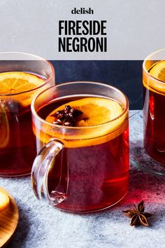 two mugs of tea with orange slices and anise on the side next to it