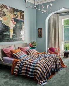 a bed sitting in a bedroom under a chandelier next to a painting on the wall