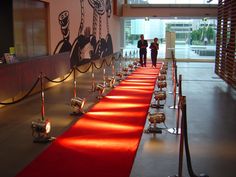 two people walking down a long red carpeted hallway with candles on each side and an artistic wall behind them