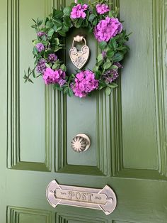 a green door with pink flowers and a heart shaped sign hanging on it's side