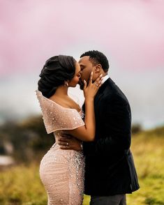 a man and woman kissing each other in front of a pink sky with clouds behind them