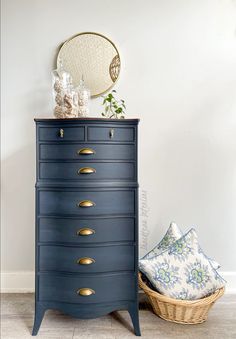 a blue dresser sitting next to a basket on top of a wooden floor in front of a white wall