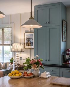 a wooden table topped with fruit and vegetables next to a kitchen light hanging over it