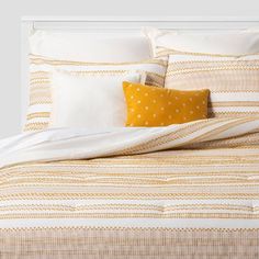 a bed with yellow and white striped comforter, pillows and pillow cases on it