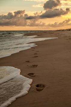 footprints in the sand on a beach at sunset