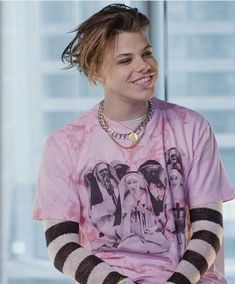 a person sitting down wearing a pink shirt with black and white stripes on the sleeves