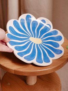 a person holding a blue and white flower shaped dish on top of a wooden table