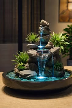 a water fountain with rocks and plants in the center on a table next to a lamp