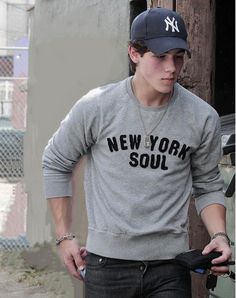 a young man wearing a new york soul sweatshirt and cap, standing in front of a building