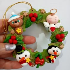 a hand holding a christmas wreath ornament with penguins and snowmen on it