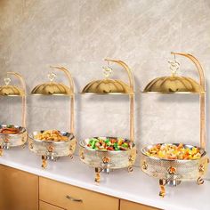 four metal bowls filled with food on top of a white counter next to gold dishes