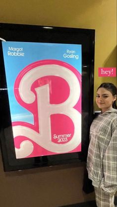 a woman standing in front of a sign with the letter b next to her is smiling at the camera