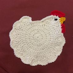 a crocheted chicken placemat on a red tablecloth with a yellow and white rooster head