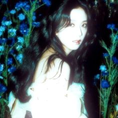 a woman with long black hair standing in front of blue flowers