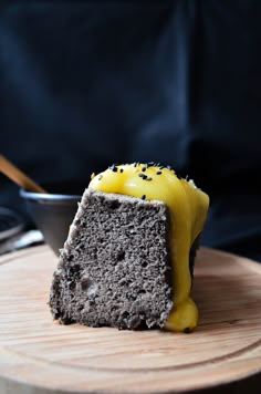 a piece of cake with yellow icing on a wooden plate next to a bowl