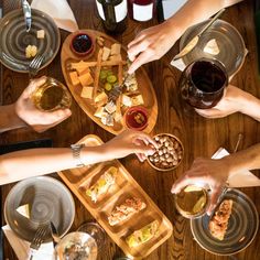 several people sitting around a wooden table with plates and glasses of wine, cheeses and crackers