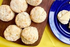 some biscuits and cheese are on a blue plate next to a wooden cutting board with yellow cloth