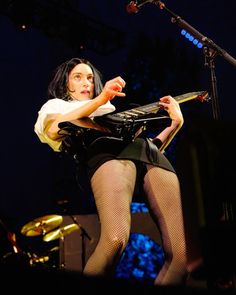 a woman in fishnet stockings and tights on stage holding a guitar with her right hand