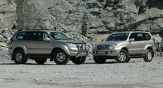 two suvs parked next to each other in front of a rocky mountain side area