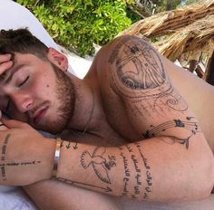 a man with tattoos on his arm and chest laying in a bed next to a straw hut