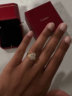 a woman's hand with an engagement ring next to a red box