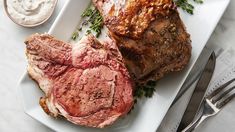 two pieces of meat on a plate next to a fork and knife with dips