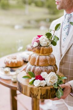 a man in a suit is holding a cake on a table with flowers and leaves