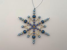 a snowflake ornament with blue beads and gold accents on a white background