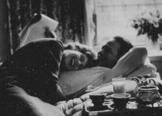 a man and woman laying in bed next to each other with coffee cups on the table