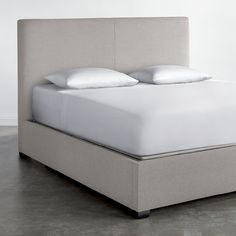 an upholstered bed with white pillows and linens