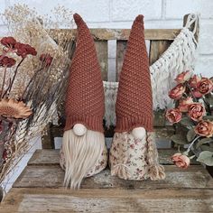 two knitted gnomes sitting on a wooden bench with dried flowers in the background