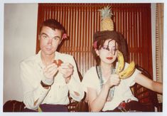 a man and woman sitting next to each other holding bananas in front of their faces