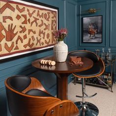 a room with blue walls and art on the wall, including a wooden table surrounded by black leather chairs