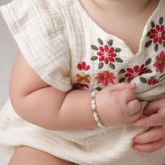 a baby is wearing a white dress with red flowers on it's chest and bracelet