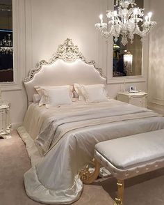 a white bed sitting under a chandelier next to a dresser with drawers on it