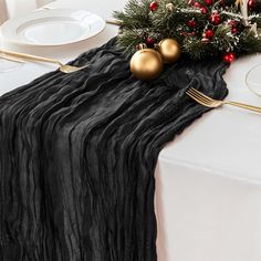 a black table runner with gold ornaments and greenery on it, next to a white plate