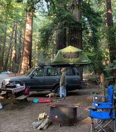 a man standing in front of a tent next to a parked car and campfire