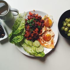 a white plate topped with meat and vegetables next to a bowl of grapes on a table