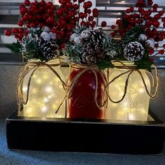 two mason jar vases with pine cones and red berries are decorated with string lights