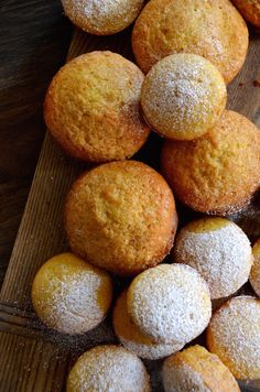 a pile of powdered sugar muffins sitting on top of a wooden cutting board